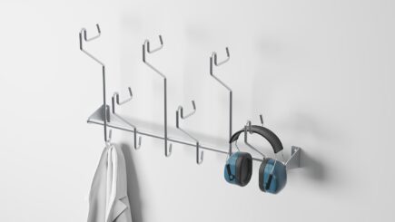 Wall-mounted stainless steel hook rack with six hooks, holding hearing protectors, helmets, and jackets, ideal for organized storage.